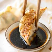 Potsticker being dipped in a small bowl with soy sauce and chilli oil
