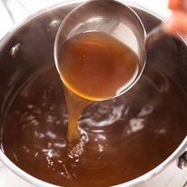 Ladle scooping up hot beef stock from pot
